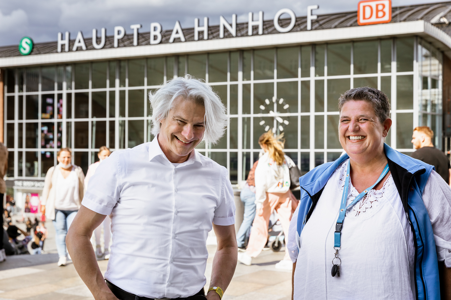 Die beiden Gesprächspartner stehen gut gelaunt vor dem Kölner Hauptbahnhof.