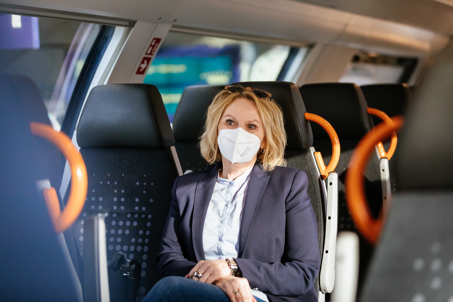 Eine Frau im Businesslook sitzt in einem Zug des Schienennahverkehrs. Ganz entspannt fährt sie zur Arbeit.